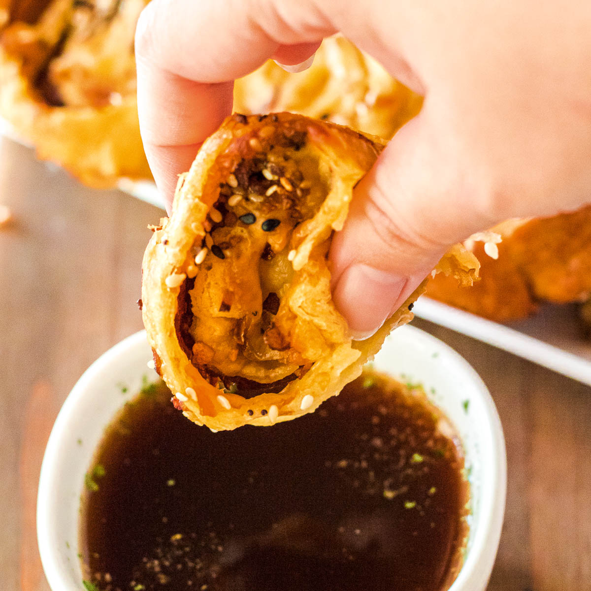 Hand dipping a golden baked French Dip Roast Beef Pinwheel into au jus.