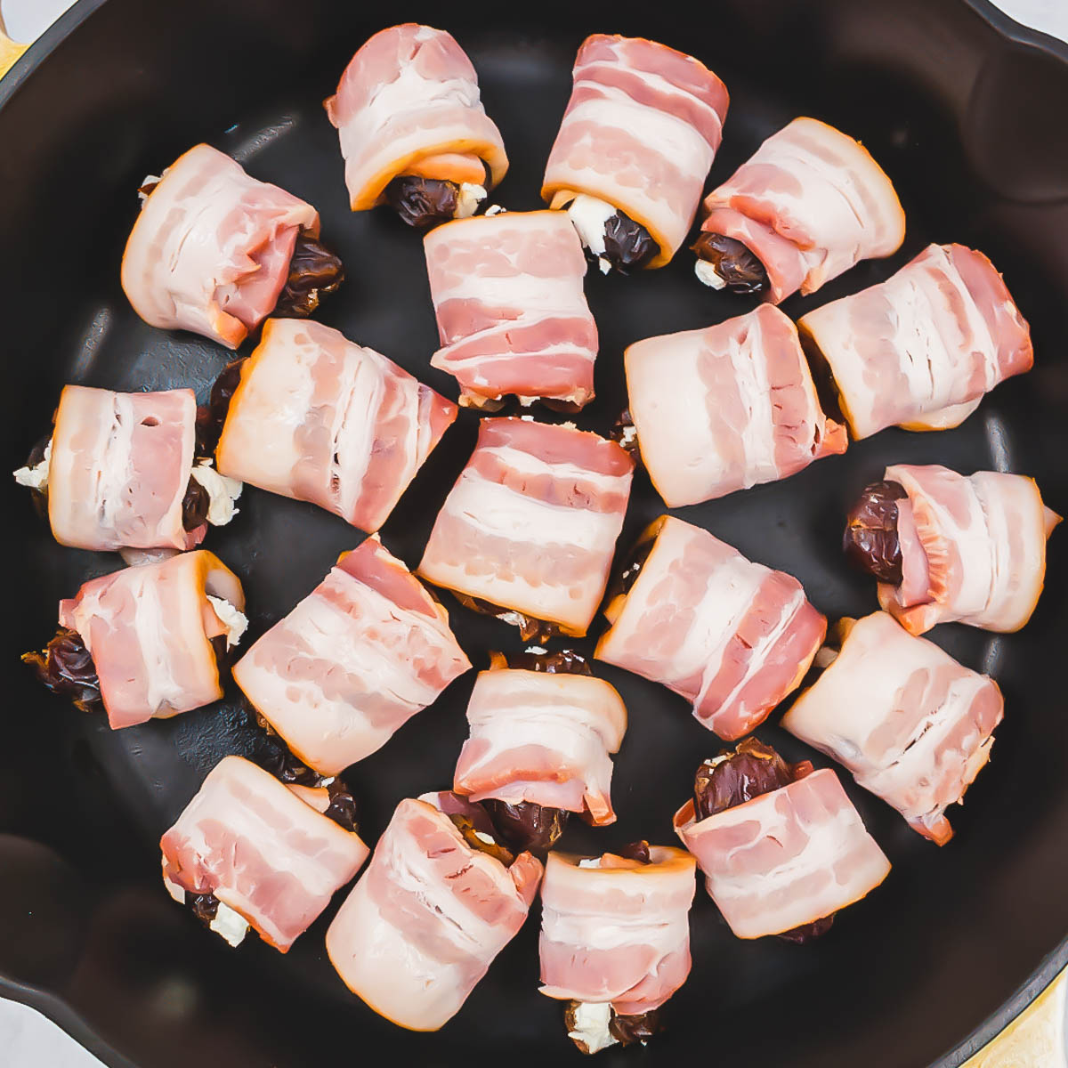 Stuffed dates wrapped in bacon about to be fried in a cast iron pan.