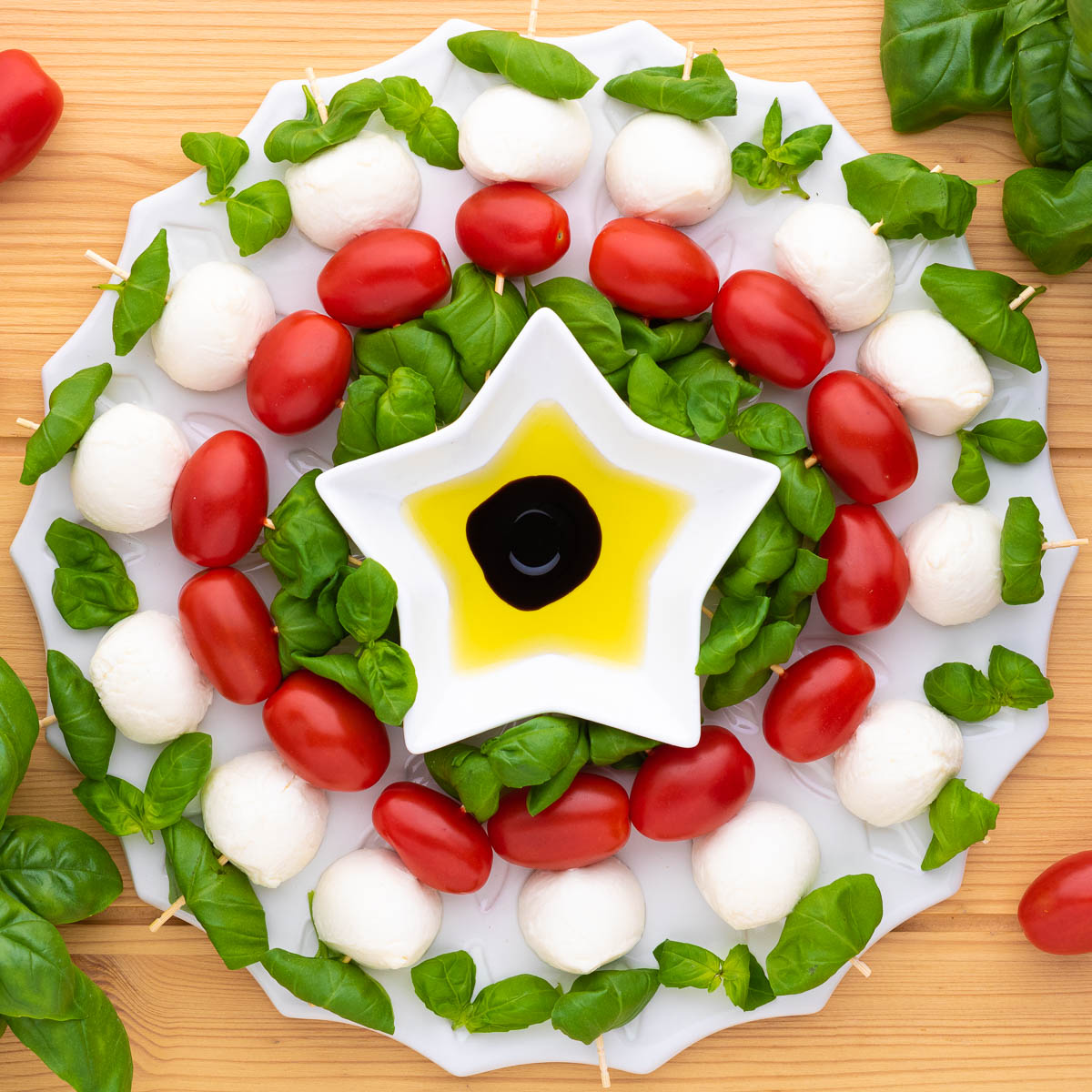 Fresh basil, bocconcini ball, and cherry tomatoes threaded onto wooden skewers and arranged into a circular caprese appetizer wreath.
