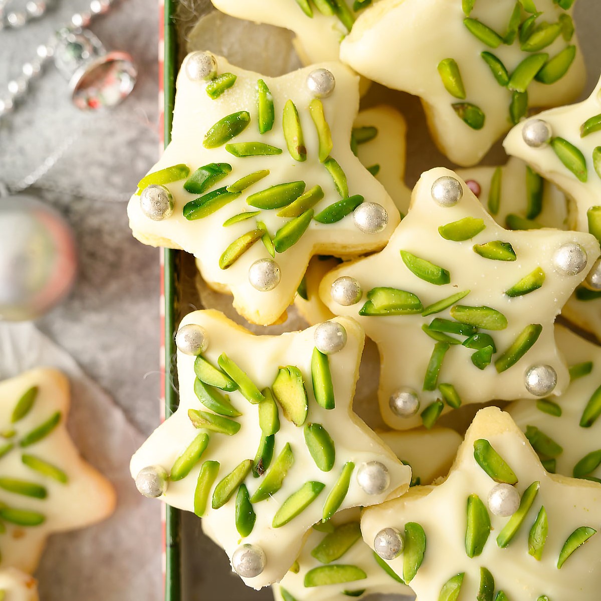 Close up of sugar star cookies decorated with pistachios and silver dragées.