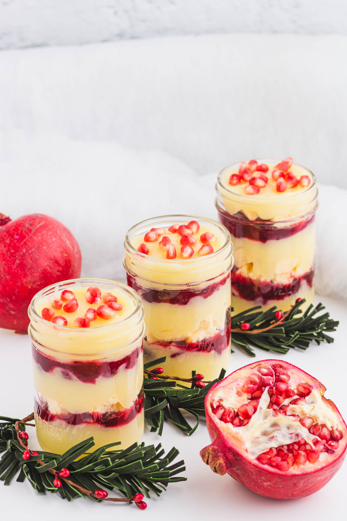 Three glass half pint jars filled with a layered Christmas trifle garnished with pomegranate seeds.