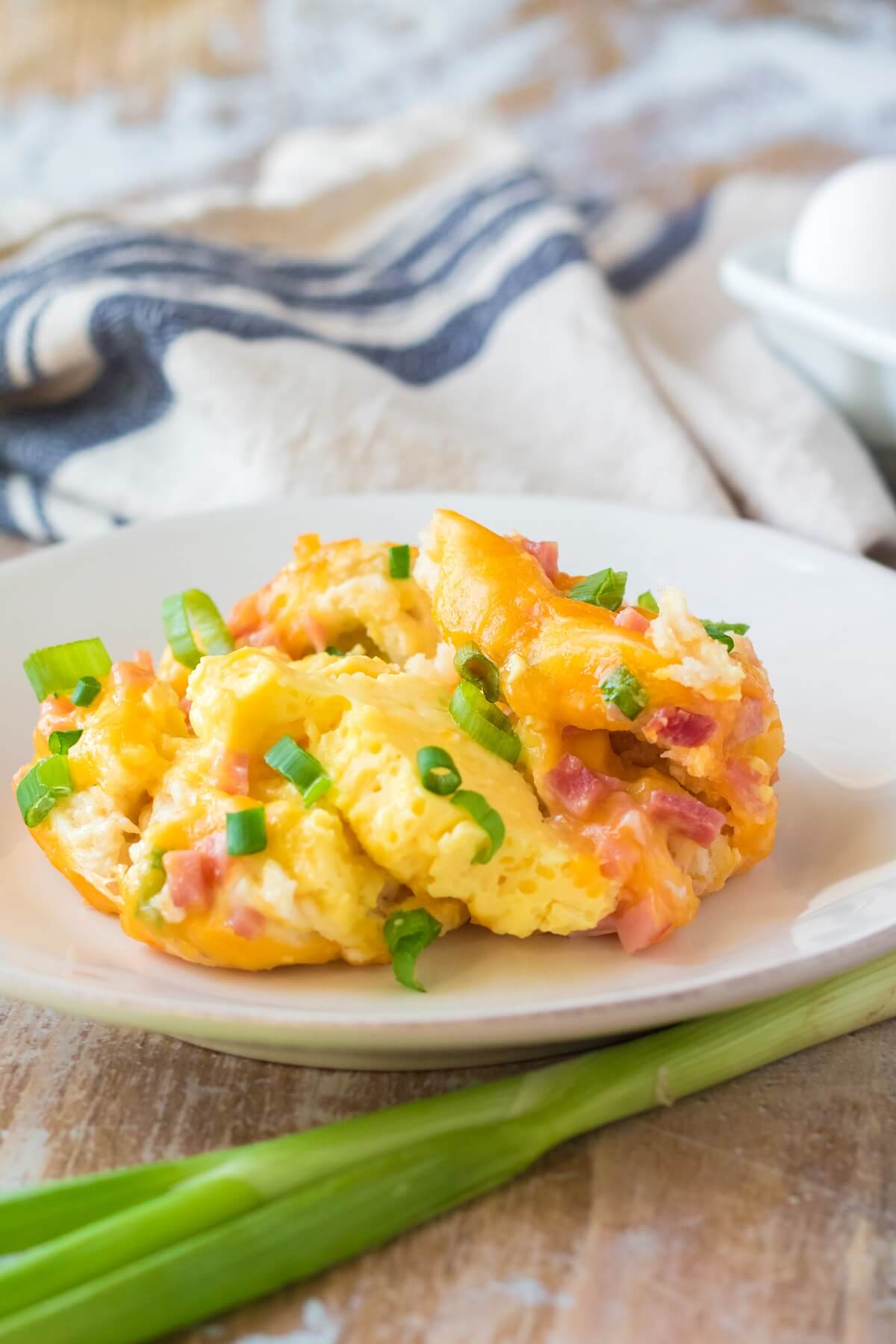 A serving of slow cooker breakfast casserole with ham, cheddar cheese, and green onions served on a white plate on a breakfast table. 