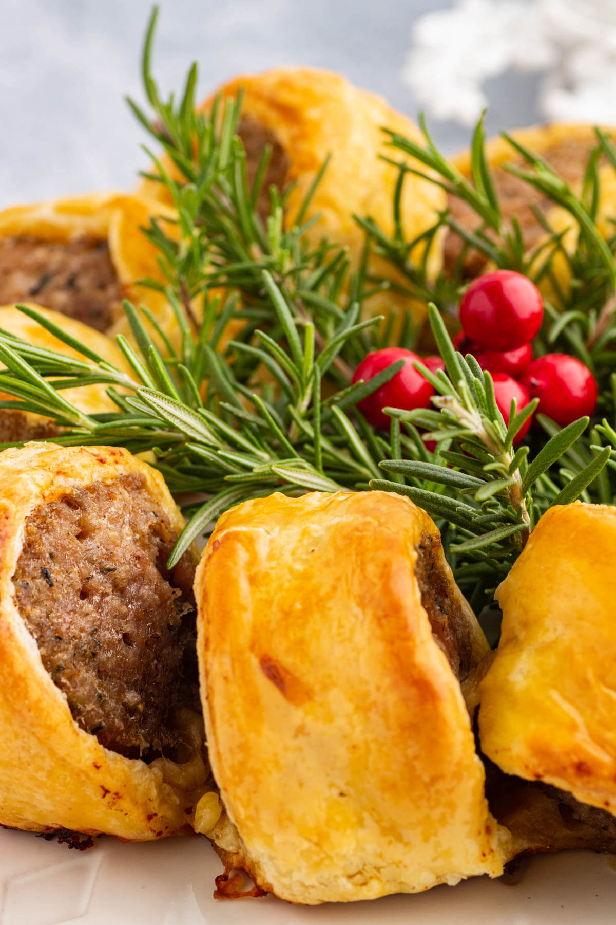 A festive golden baked sausage roll wreath garnished with fresh rosemary and cranberries.