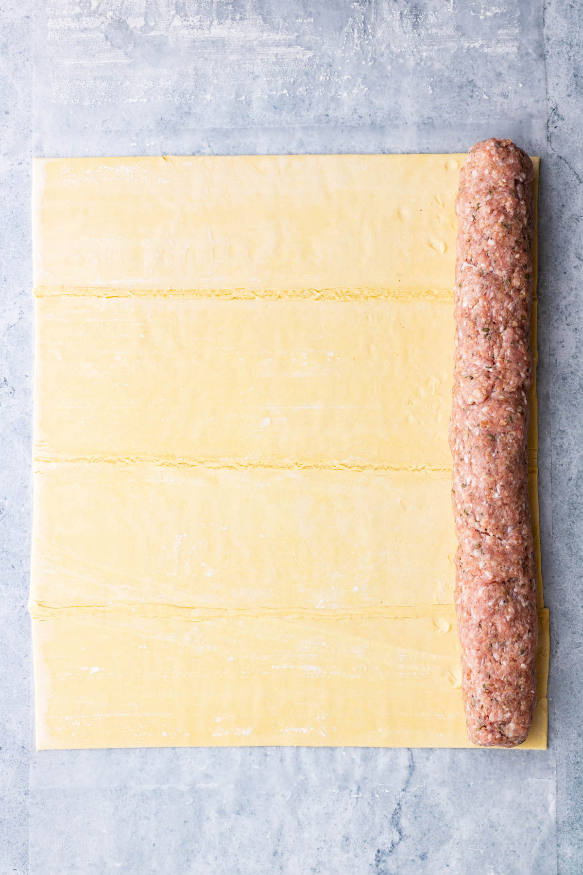 A sheet of puff pastry with a log of pork sausage meat down the length of one side.