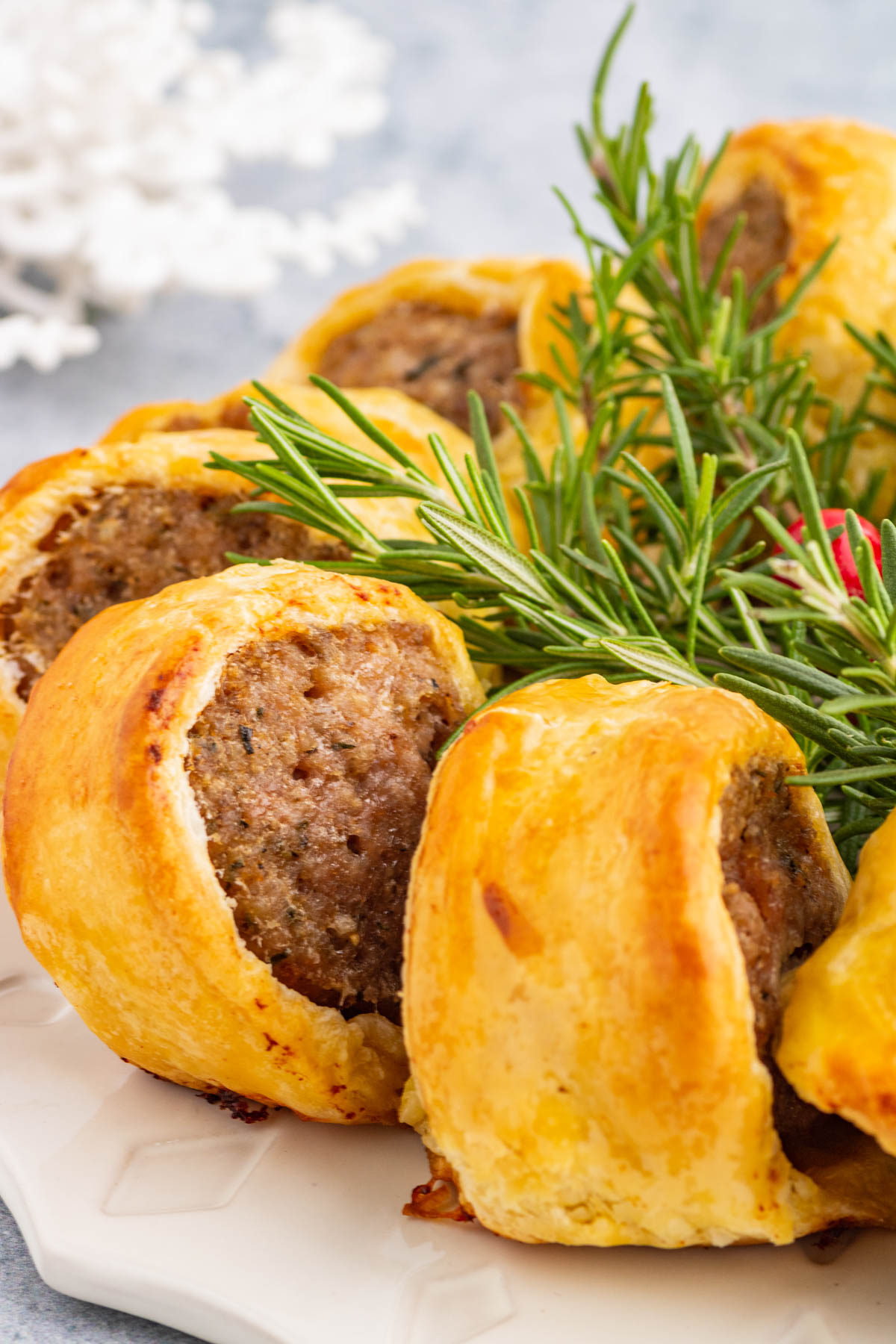 A festive golden baked sausage roll wreath garnished with fresh rosemary.