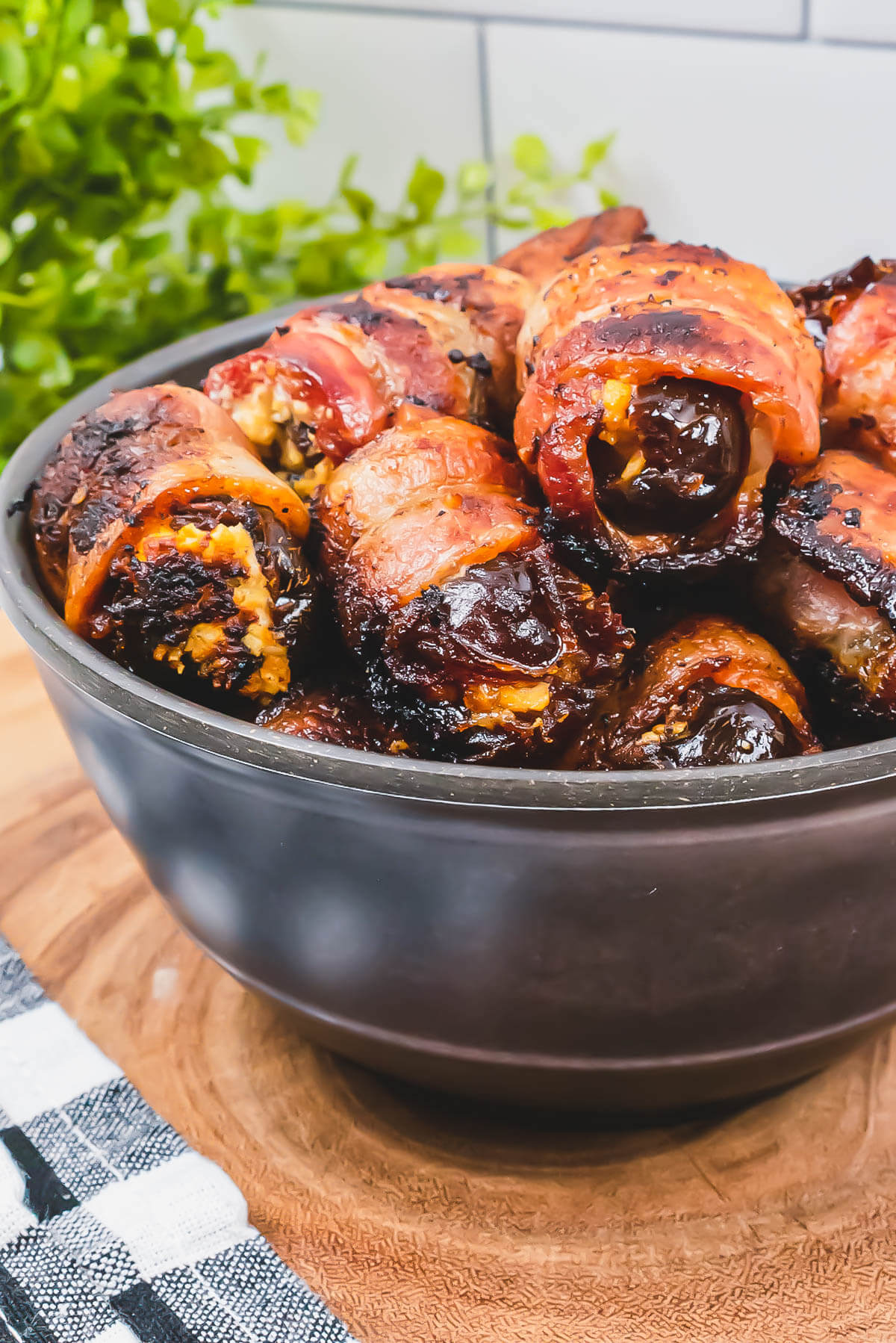 A bowl of glistening bacon wrapped stuffed dates on a wooden board.