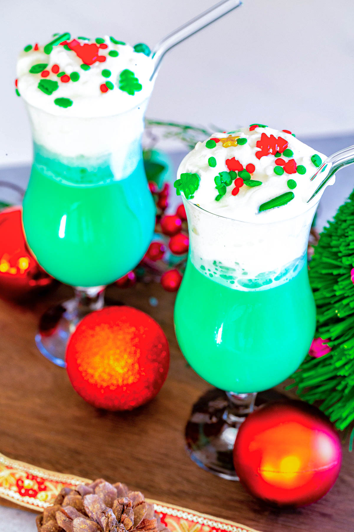Two hurricane glasses filled with blue hawaiian cocktail topped with whipped cream and christmas sprinkles.