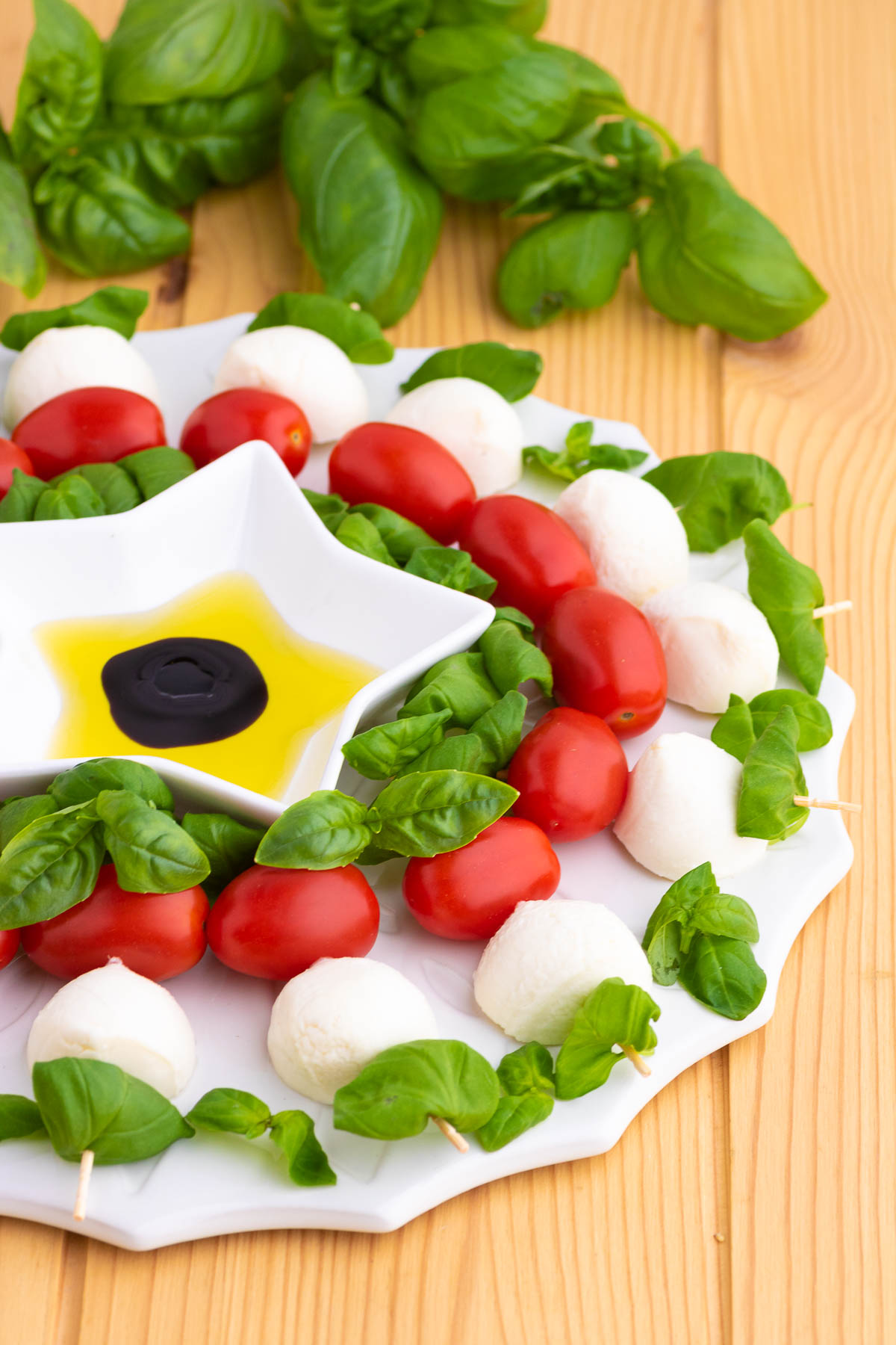 Fresh basil, bocconcini ball, and cherry tomatoes threaded onto wooden skewers and arranged into a circular caprese appetizer wreath.