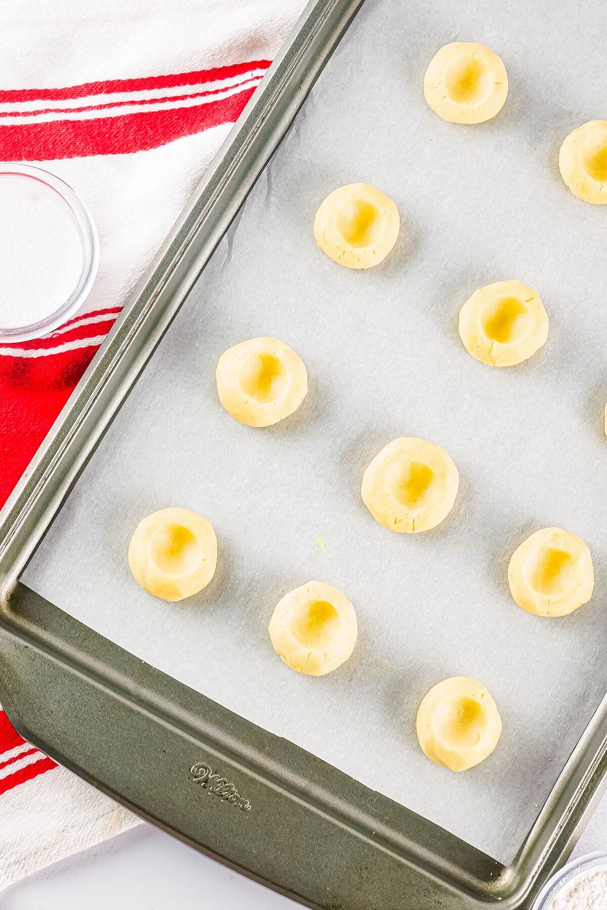 Unbaked and unfilled thumbprint cookies on a parchment lined baking sheet.
