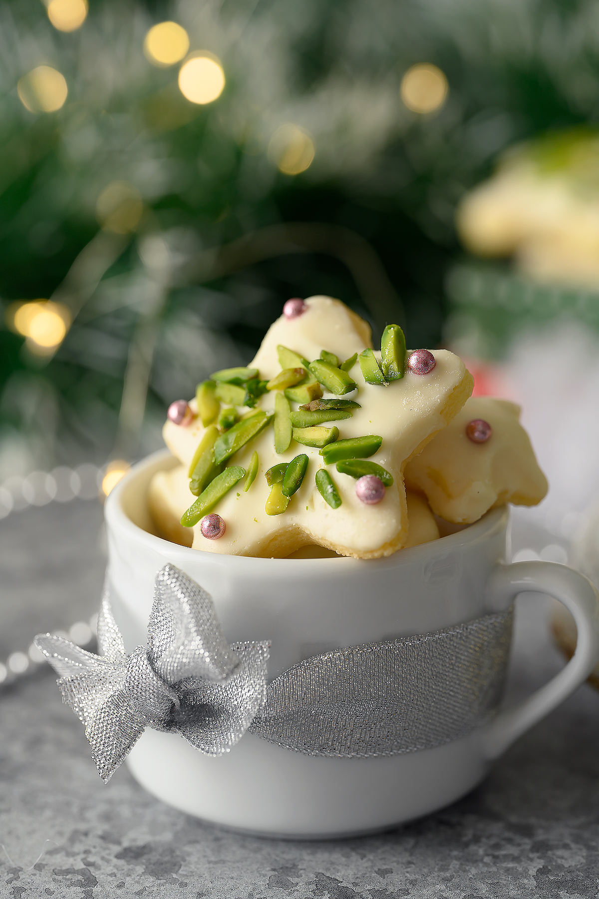 A tea cup filled with sugar star cookies decorated with pistachios and silver dragées.