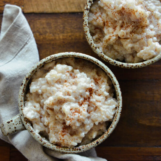 Two speckled pottery mugs filled with creamy old fashioned rice pudding dusted with cinnamon.