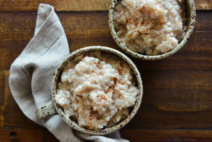 Two speckled pottery mugs filled with creamy old fashioned rice pudding dusted with cinnamon.