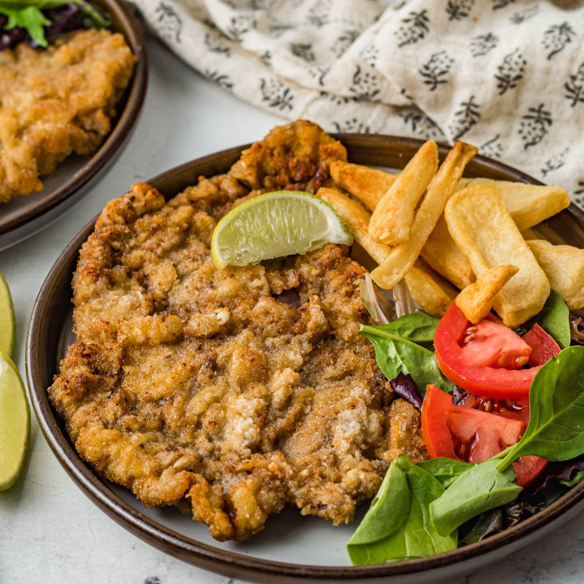 A plate full of golden fried Milanesa de res with chips and a salad.