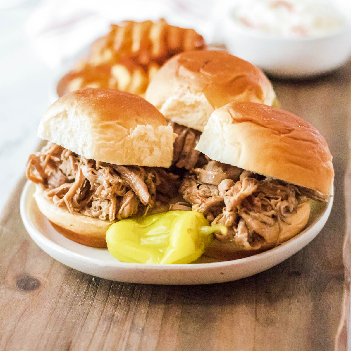 Three buns filled with shredded Mississippi Pork Roast on a white plate.