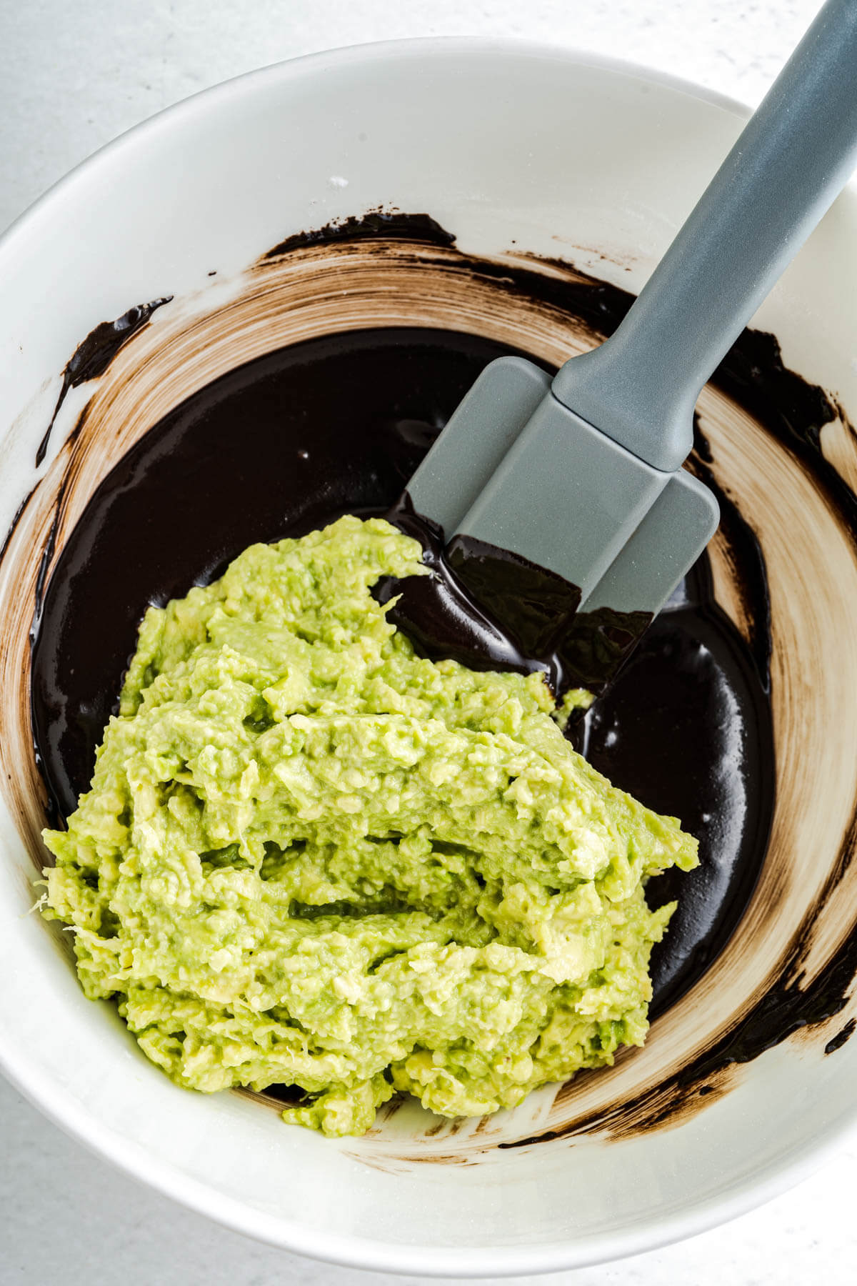 A white mixing bowl with melted chocolate and mashed green avocado.