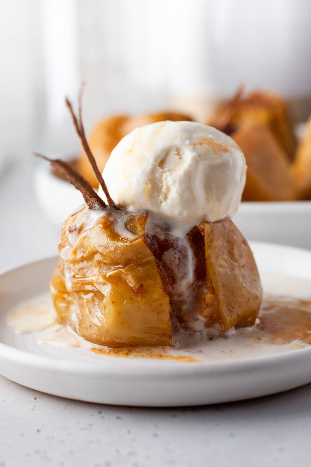 A Baked Cinnamon apple on a white plate topped with a scoop of vanilla ice cream.