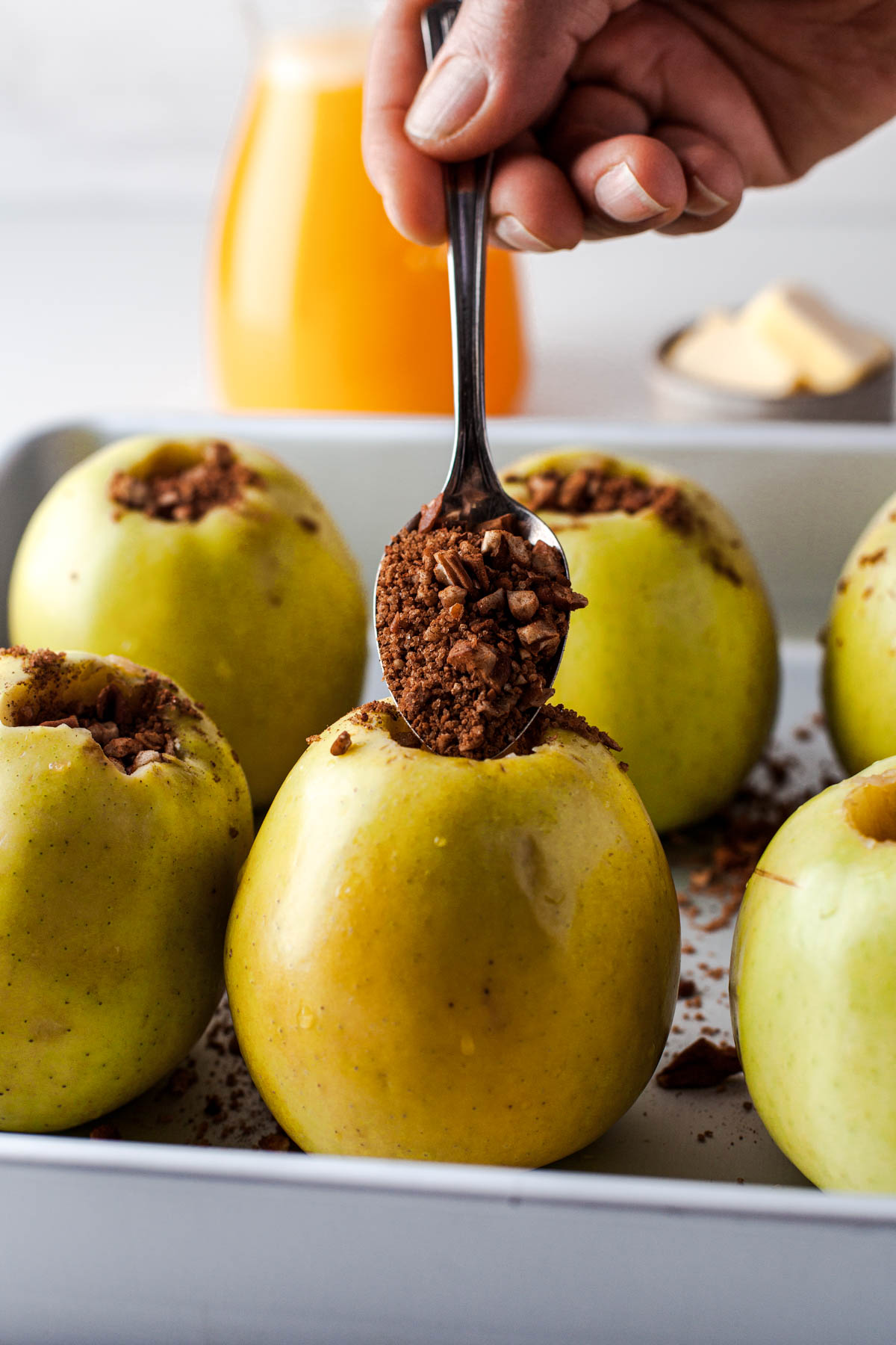 A spoon drops crumble filling into an unbaked green apple.