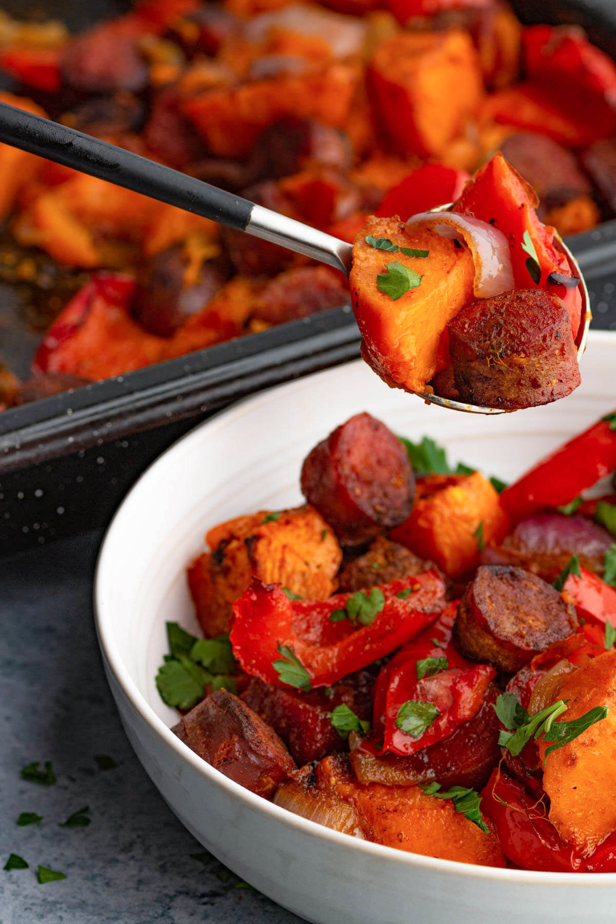A spoon holds brightly coloured chorizo sausage and veggies over a bowl of the same.