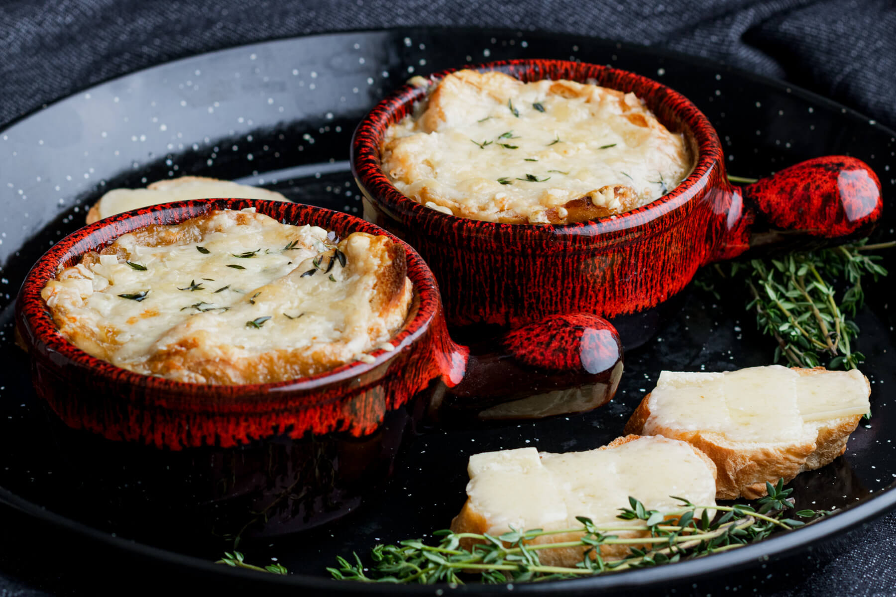 Two cheese topped bowls of French Onion soup in stunning pottery soup bowls.