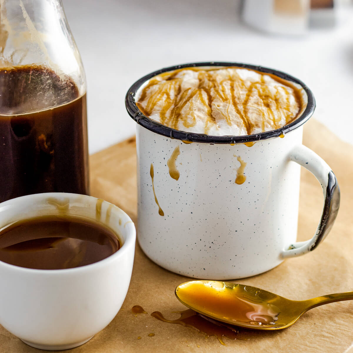 A white mug holds a foamy Caramel Macchiato garnished with a golden caramel drizzle.