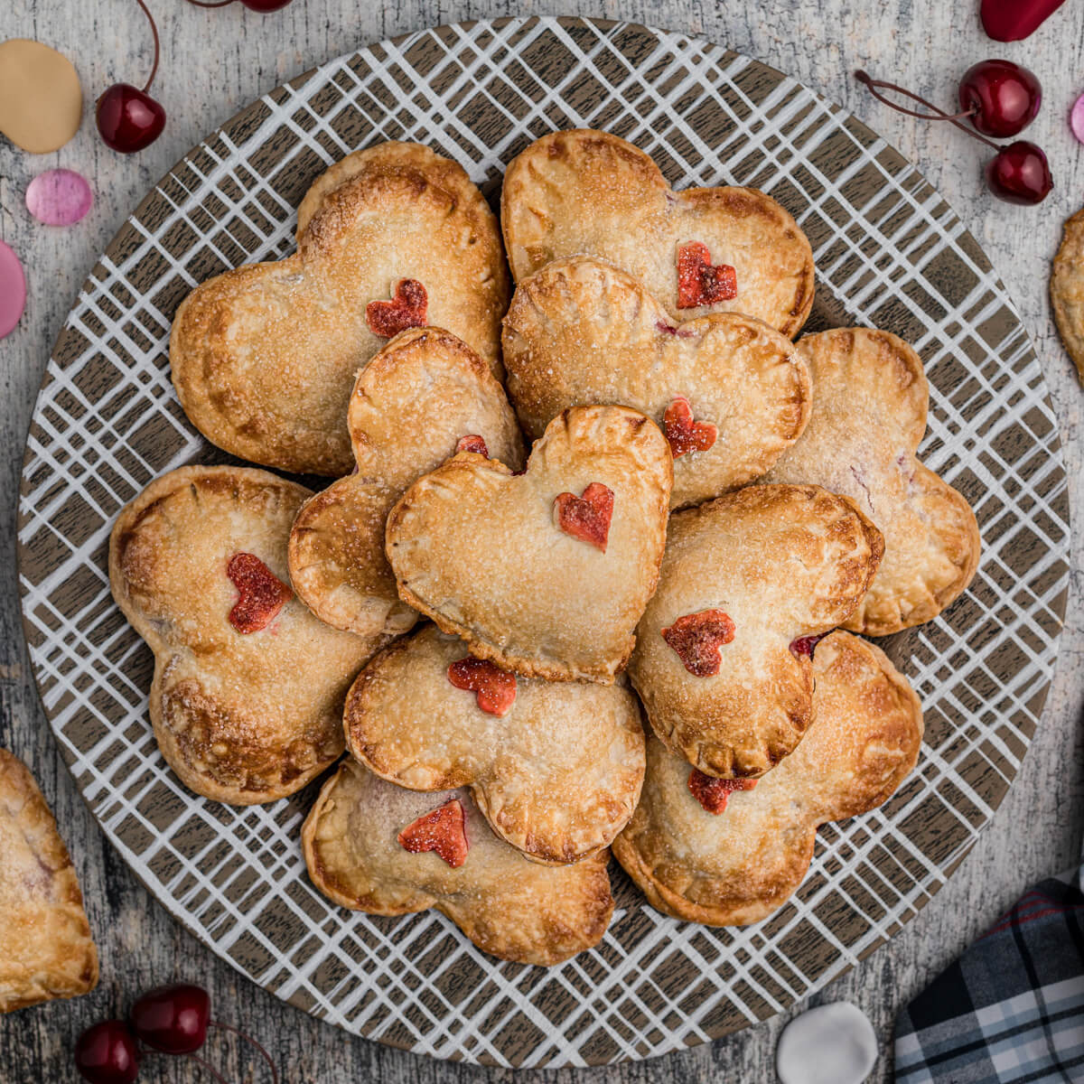 A plate full of golden baked heart shaped individual cherry hand pies decorated with red pastry hearts.