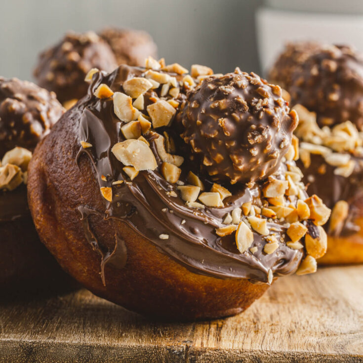 One mouthwatering Nutella donut topped with a ferrero rocher chocolate on a wooden board.