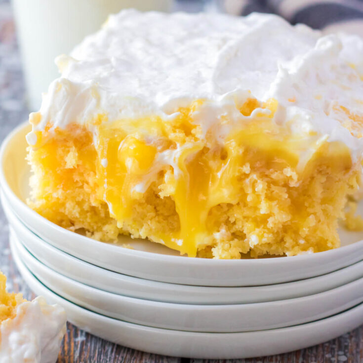 A square of dreamy Pineapple Poke Cake with creamy whipped topping on a stack of white plates.