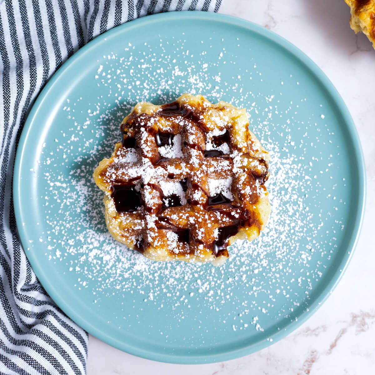 One Belgian Liège Waffle with confectioners' sugar and chocolate sauce sitting on a blue plate.