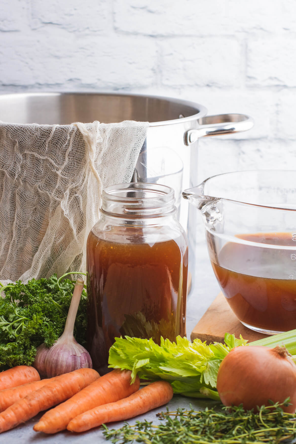 A glass quart jar filled with beef stock surrounded by fresh vegetables.