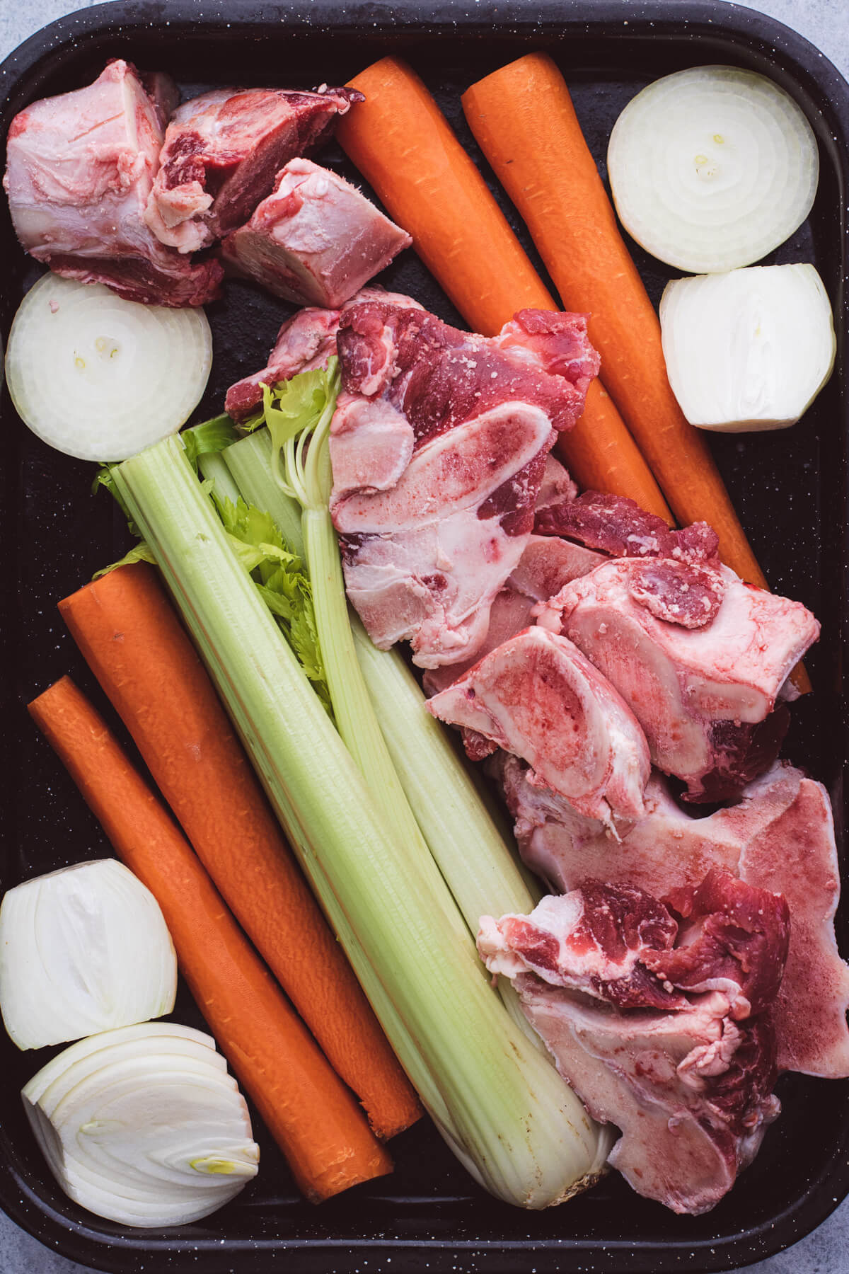 A roasting pan filled with raw veggies and meaty beef soup bones.