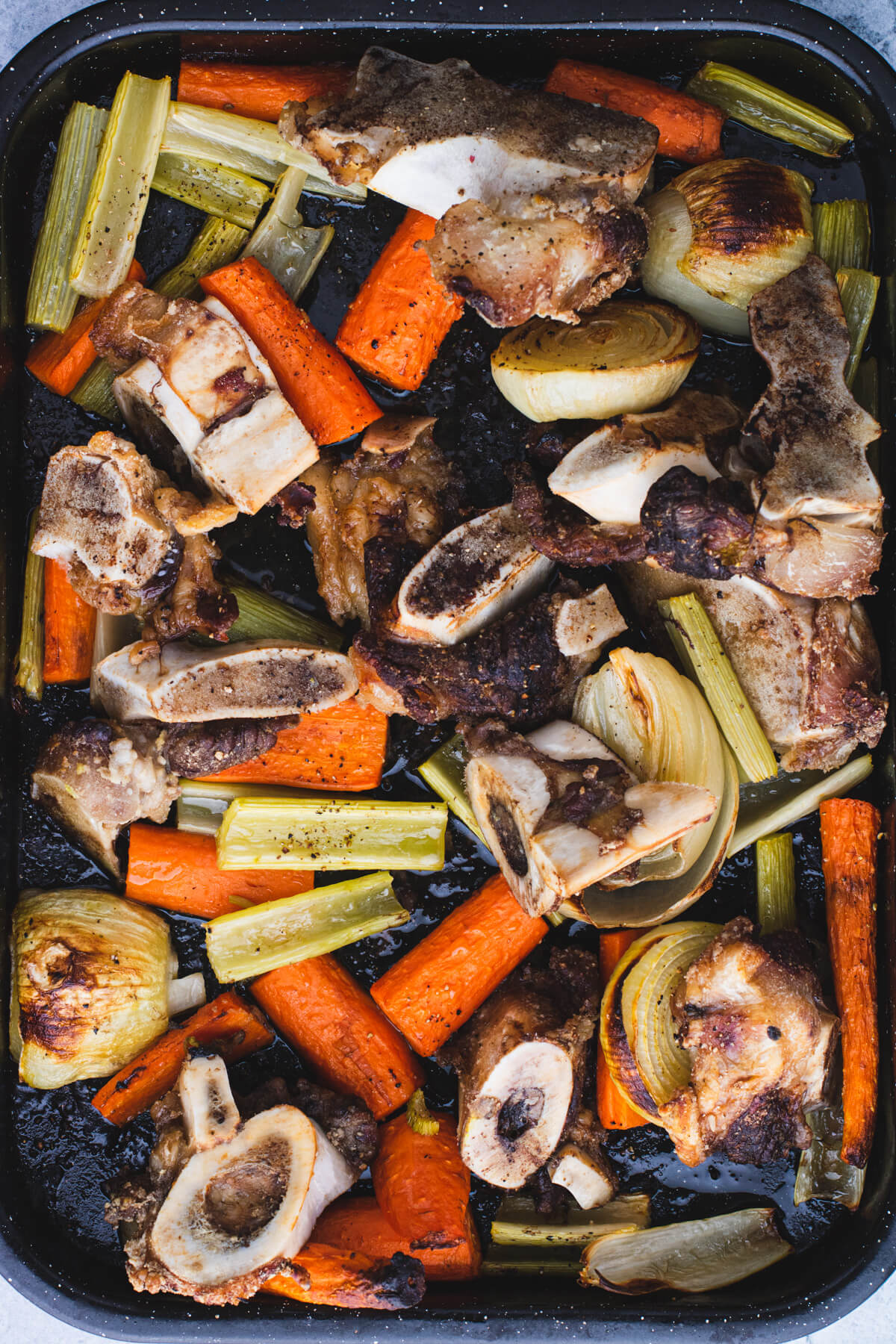 A dark pan filled with roasted vegetables and beef bones.