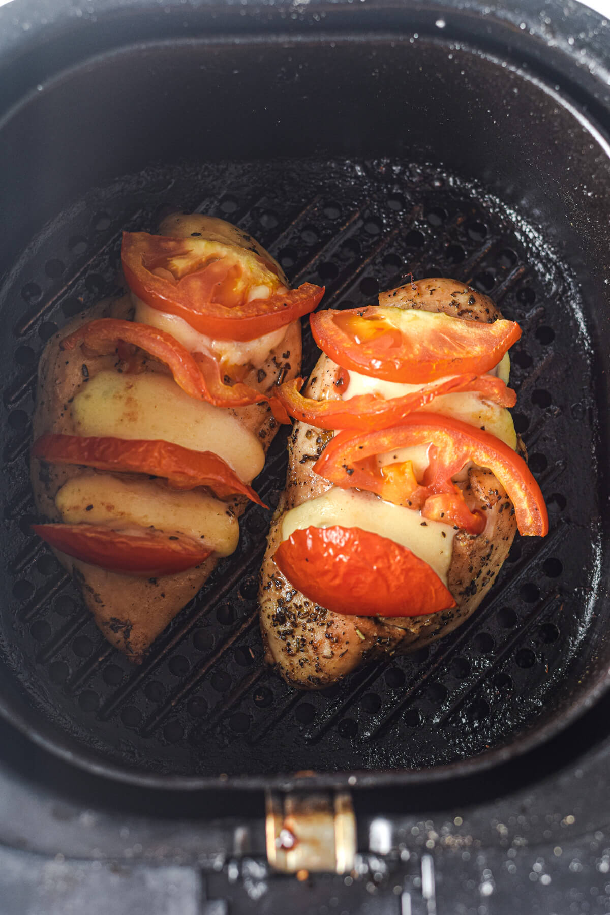 Two cooked chicken breasts stuffed with tomato and mozzarella slices in an air fryer.