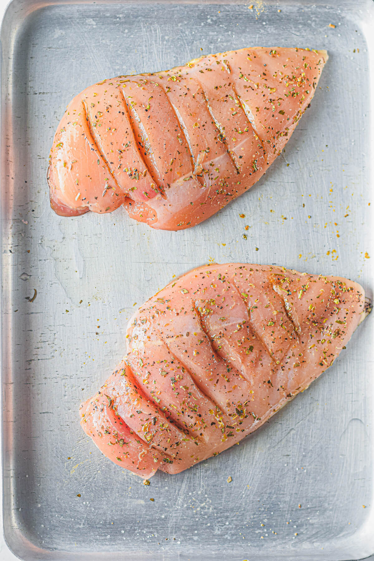 Two seasoned raw chicken breasts with slices along the top.