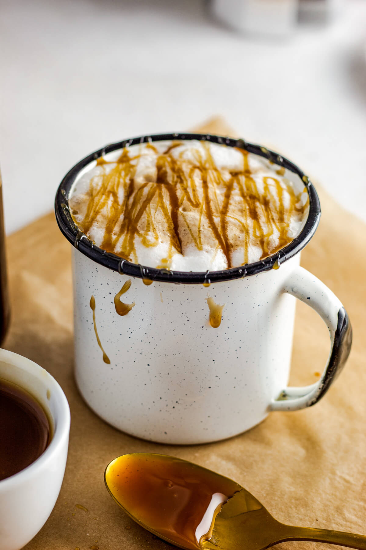 A white mug holds a foamy Caramel Macchiato garnished with a golden caramel drizzle.