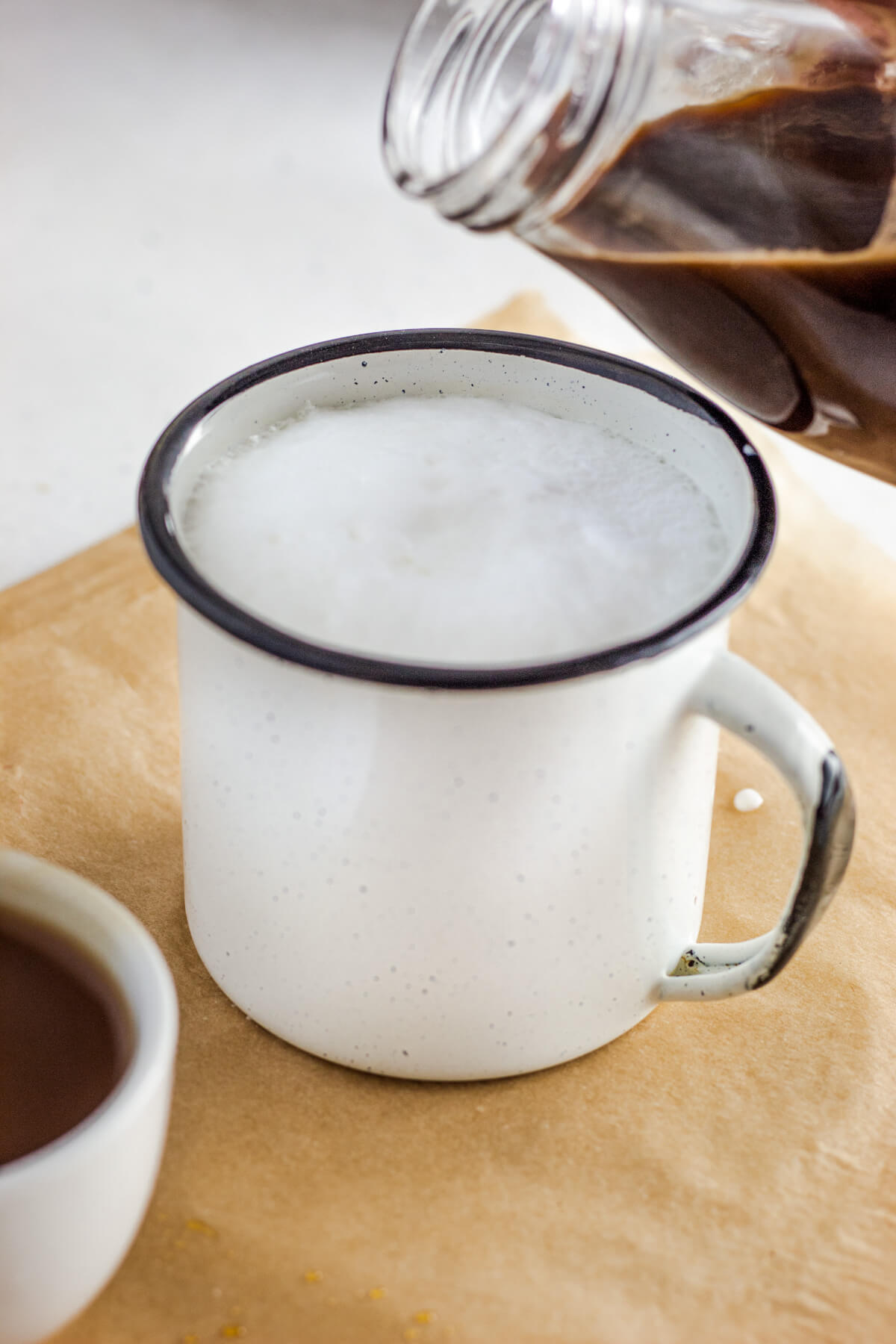 Hot espresso being poured into a white mug filled with frothy hot milk.