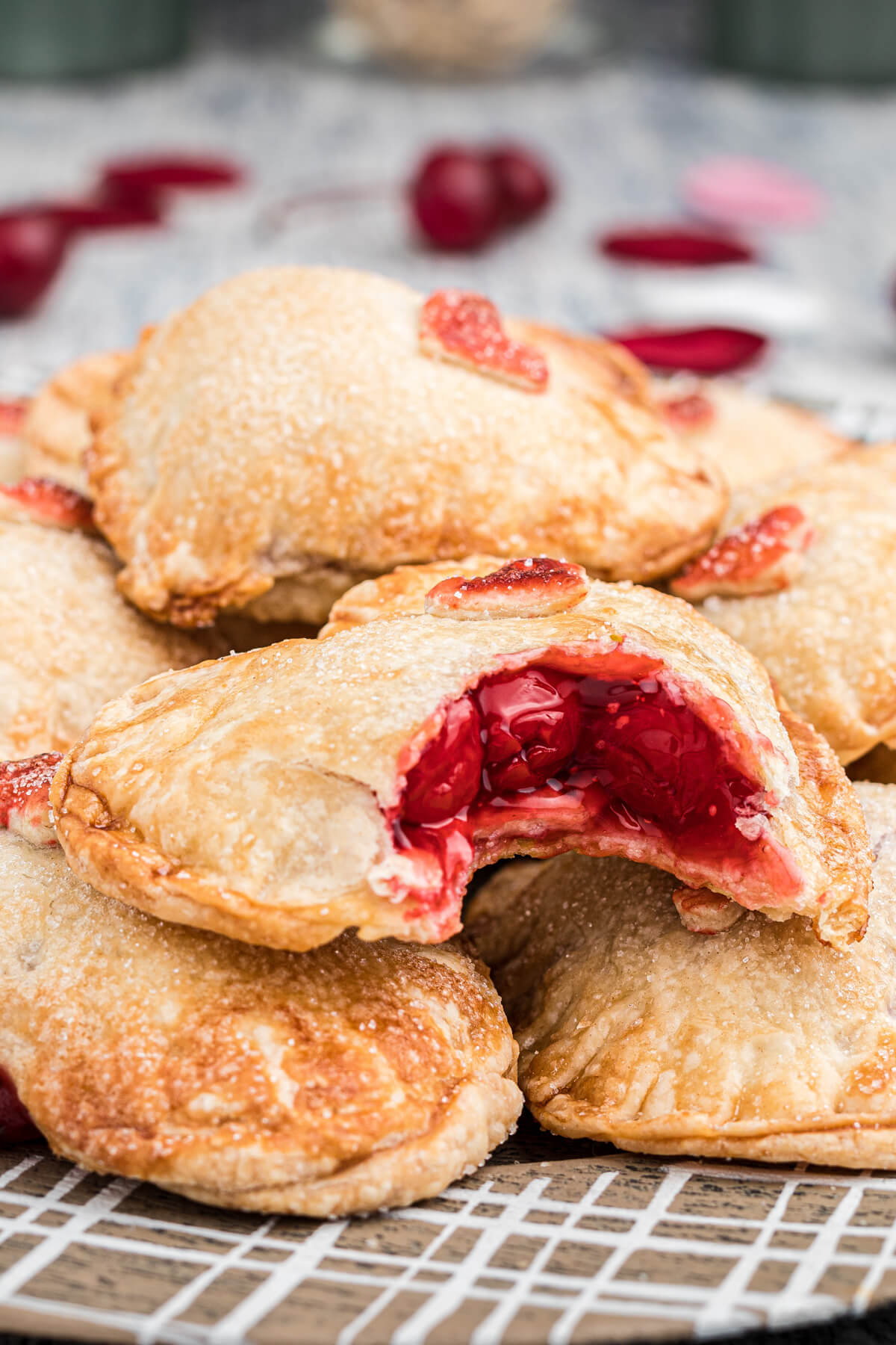 A stack of heart shaped individual cherry hand pies with a bite taken out of one showing the cherry pie filling.