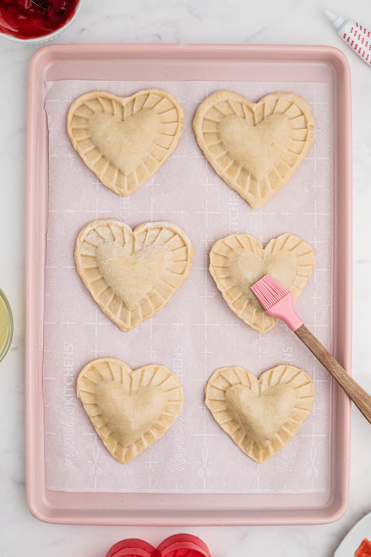 A pink baking sheet full of unbaked heart shaped individual cherry hand pies.