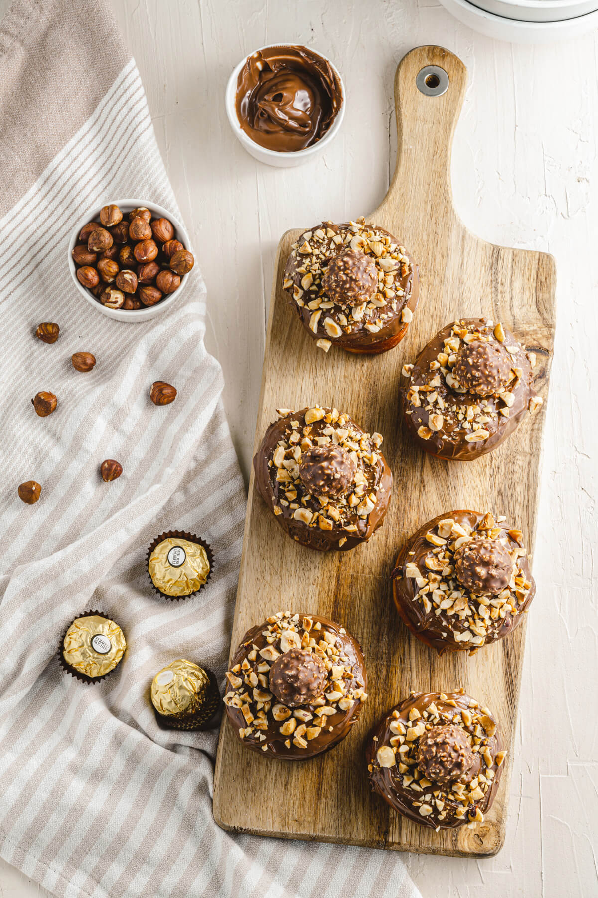 A wooden board with five ferrero rocher topped nutella donuts.