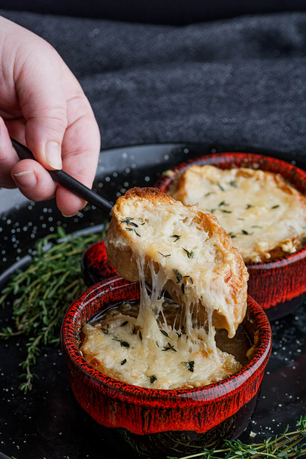 A cheese covered baguette slice being lifted out of a bowl of French Onion Soup.