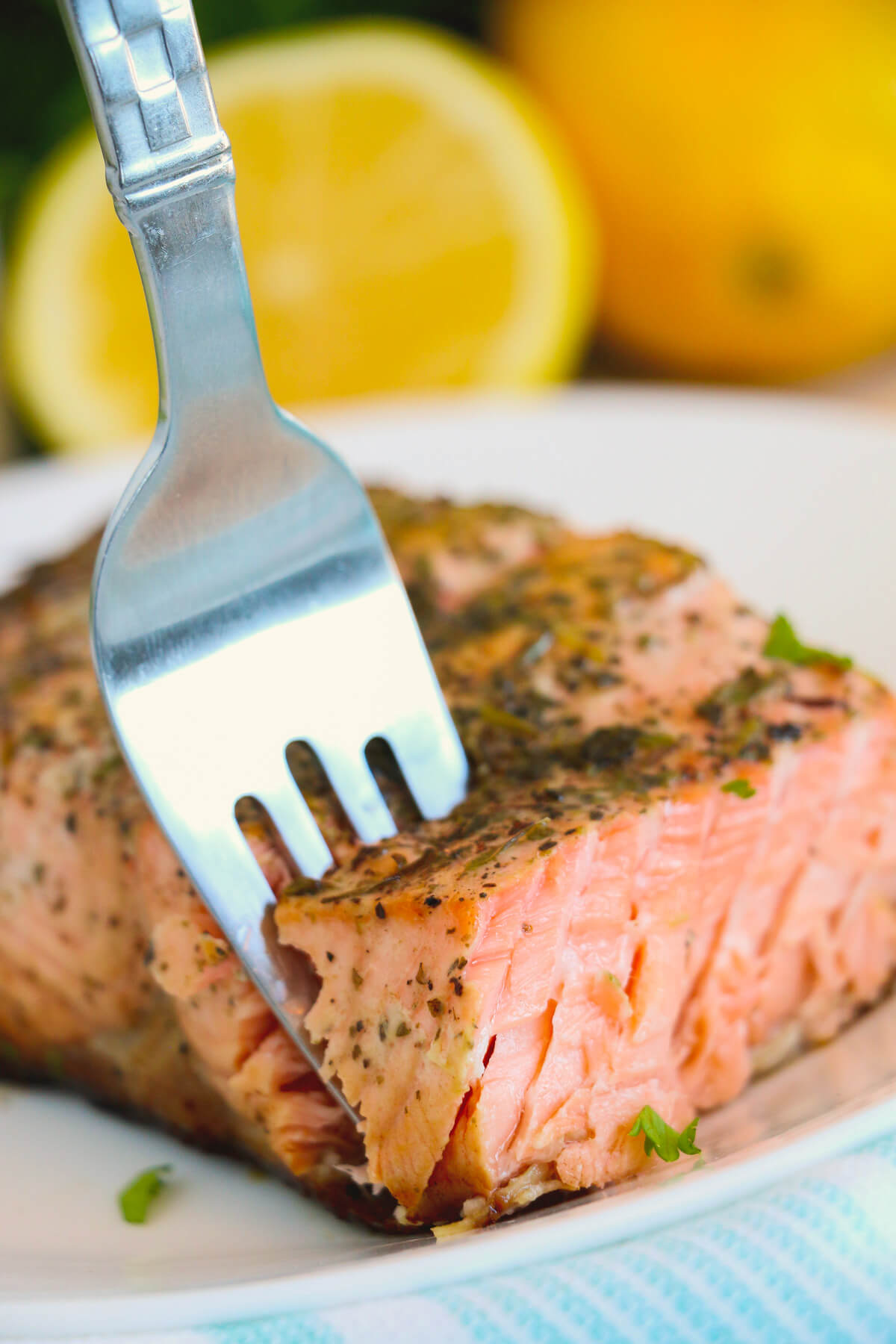 A fork with a bite of perfectly cooked skin on cast iron salmon with lemon and herbs.