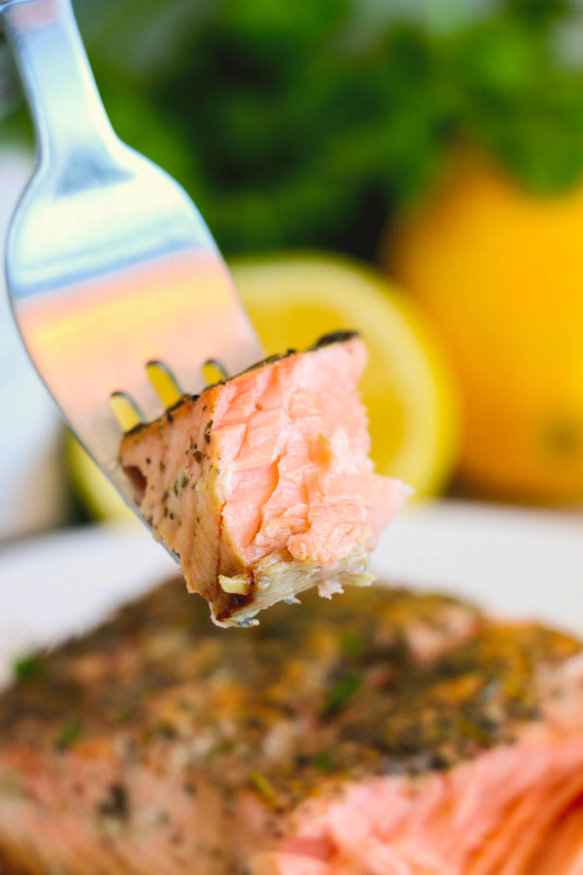 A fork with a bite of perfectly cooked skin on cast iron salmon with lemon and herbs.