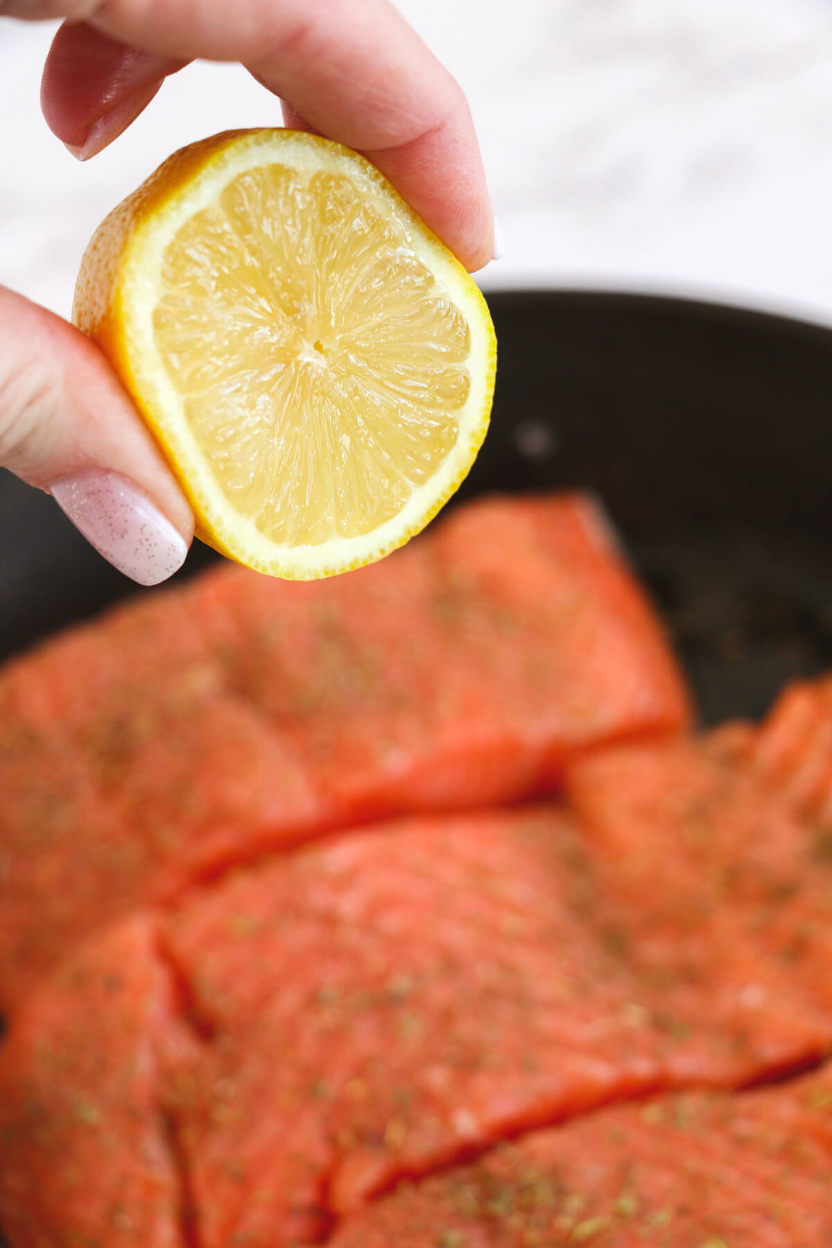 Fresh lemon juice being squeezed over three skin on salmon fillets in a cast iron skillet.