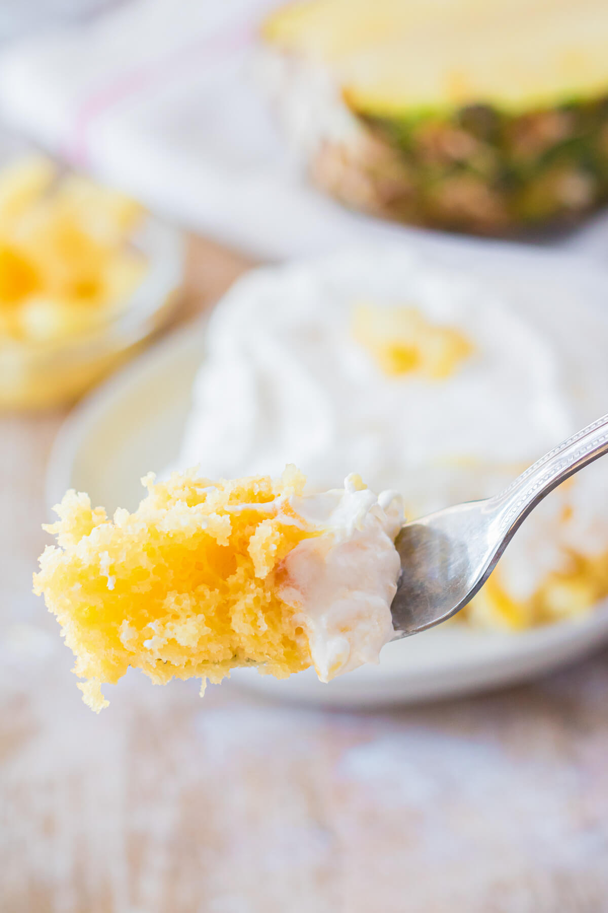 A fork holds a bite of cake in front of a square of dreamy Pineapple Poke Cake.