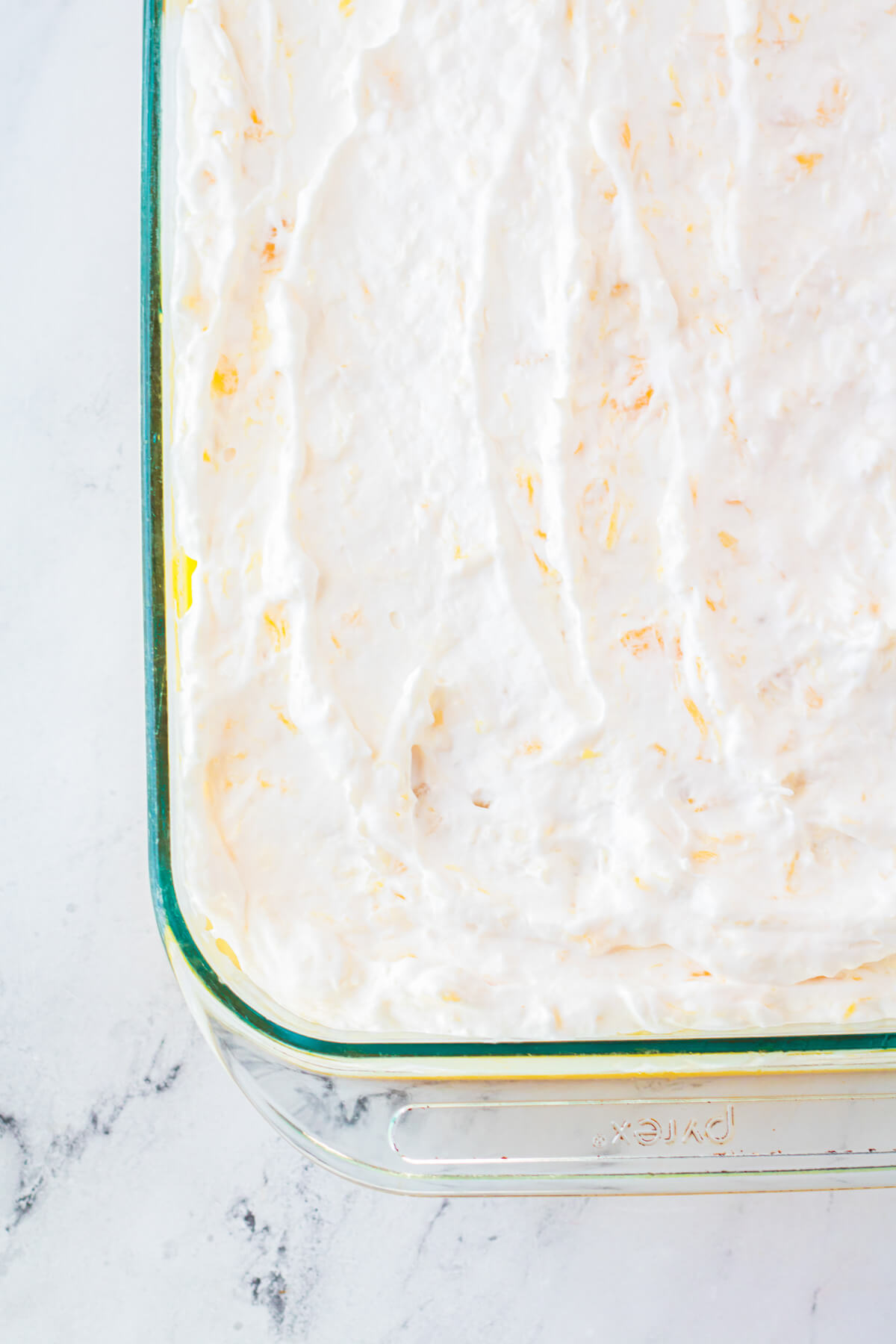 A glass baking dish of dreamy Pineapple Poke Cake with creamy whipped topping.