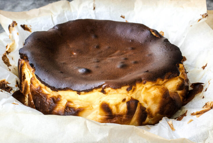 A fully baked, dark, and rustic Burnt Basque Cheesecake sitting on crumpled parchment paper.
