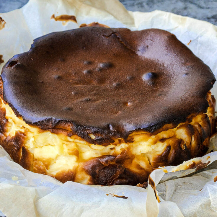 A fully baked, dark, and rustic Burnt Basque Cheesecake sitting on crumpled parchment paper.
