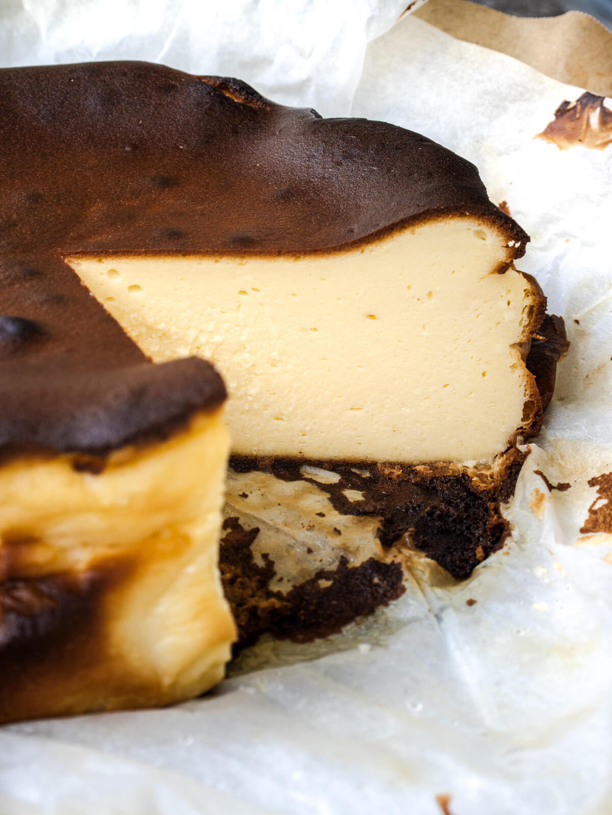 A fully baked, dark, and rustic Burnt Basque Cheesecake sitting on crumpled parchment paper with a slice missing.