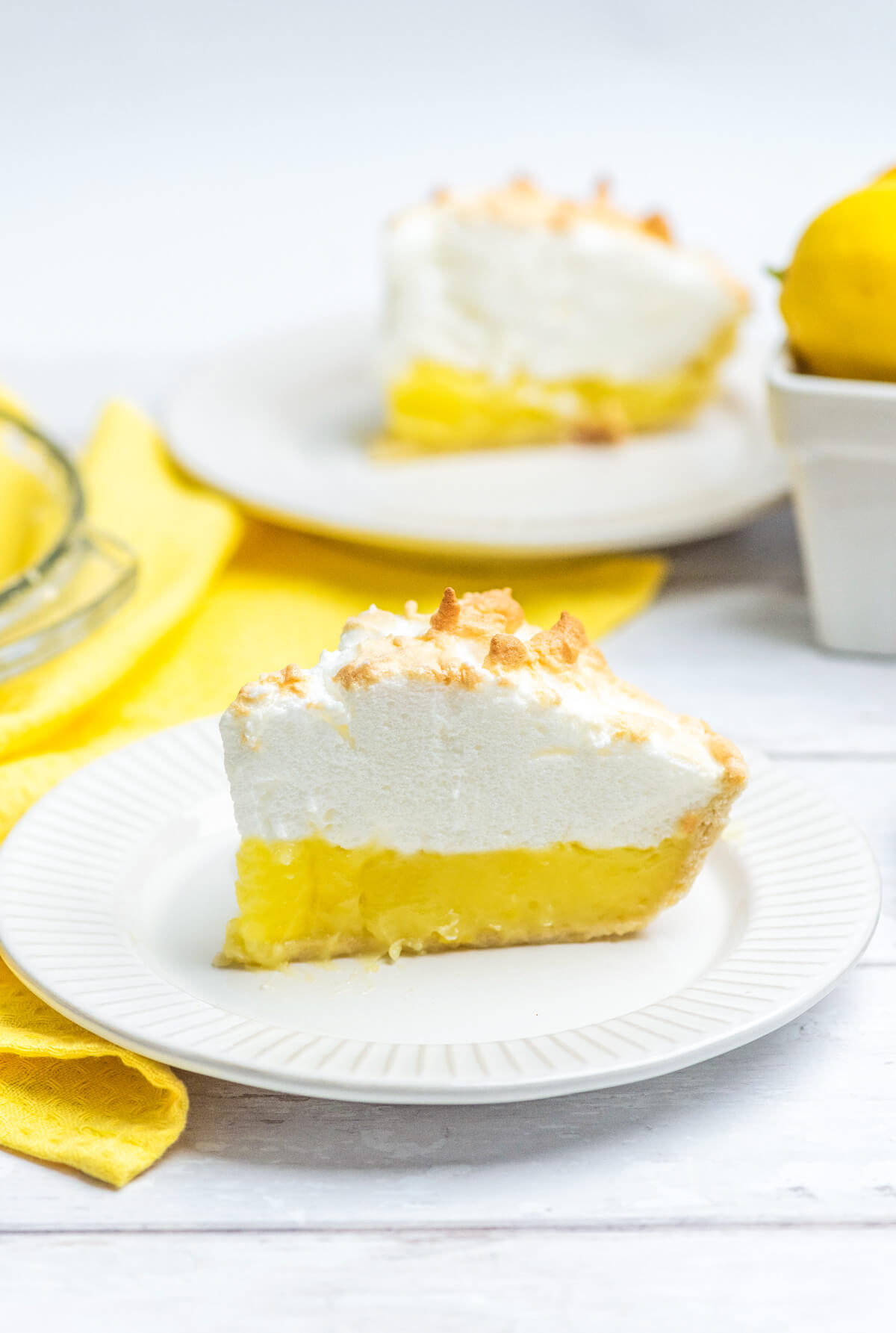 Two slices of lemon meringue pie on white plates with a yellow napkin. 