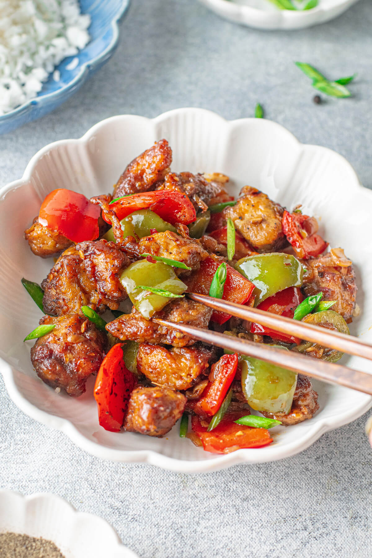 A white bowl with chopsticks containing colourful Black Pepper Chicken and vegetable stir fry.
