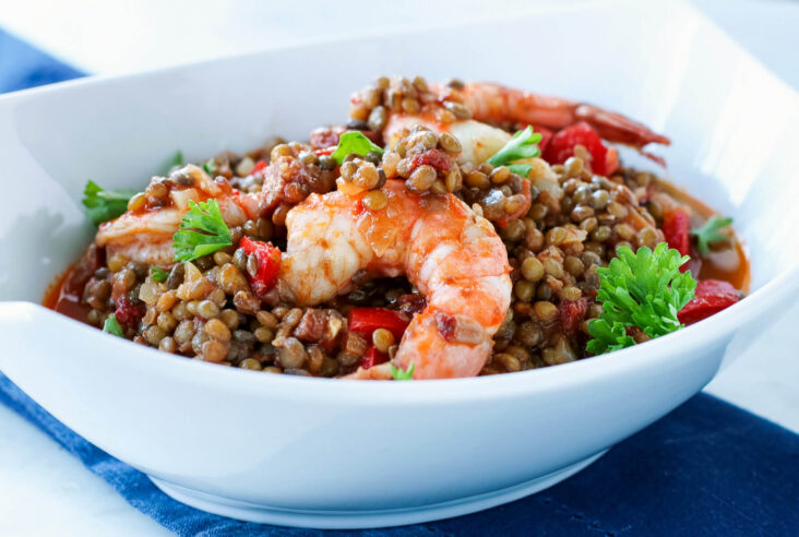 Brown lentils, red peppers, tomatoes, chorizo and shrimp in a white bowl.